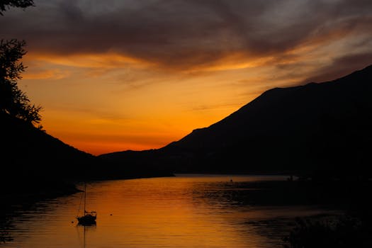 A tranquil scene of a sailboat silhouetted against a vibrant sunset over a calm lake.