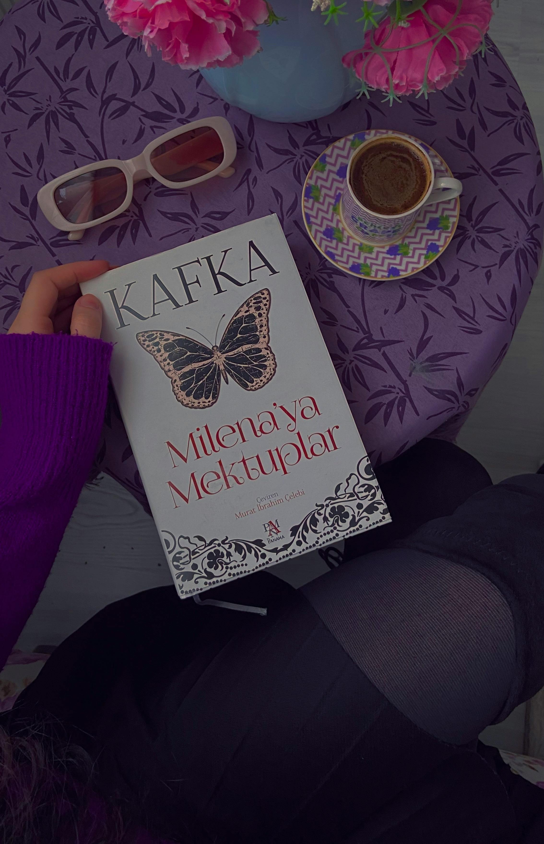 Top view of a book, coffee, and sunglasses on a floral tablecloth.