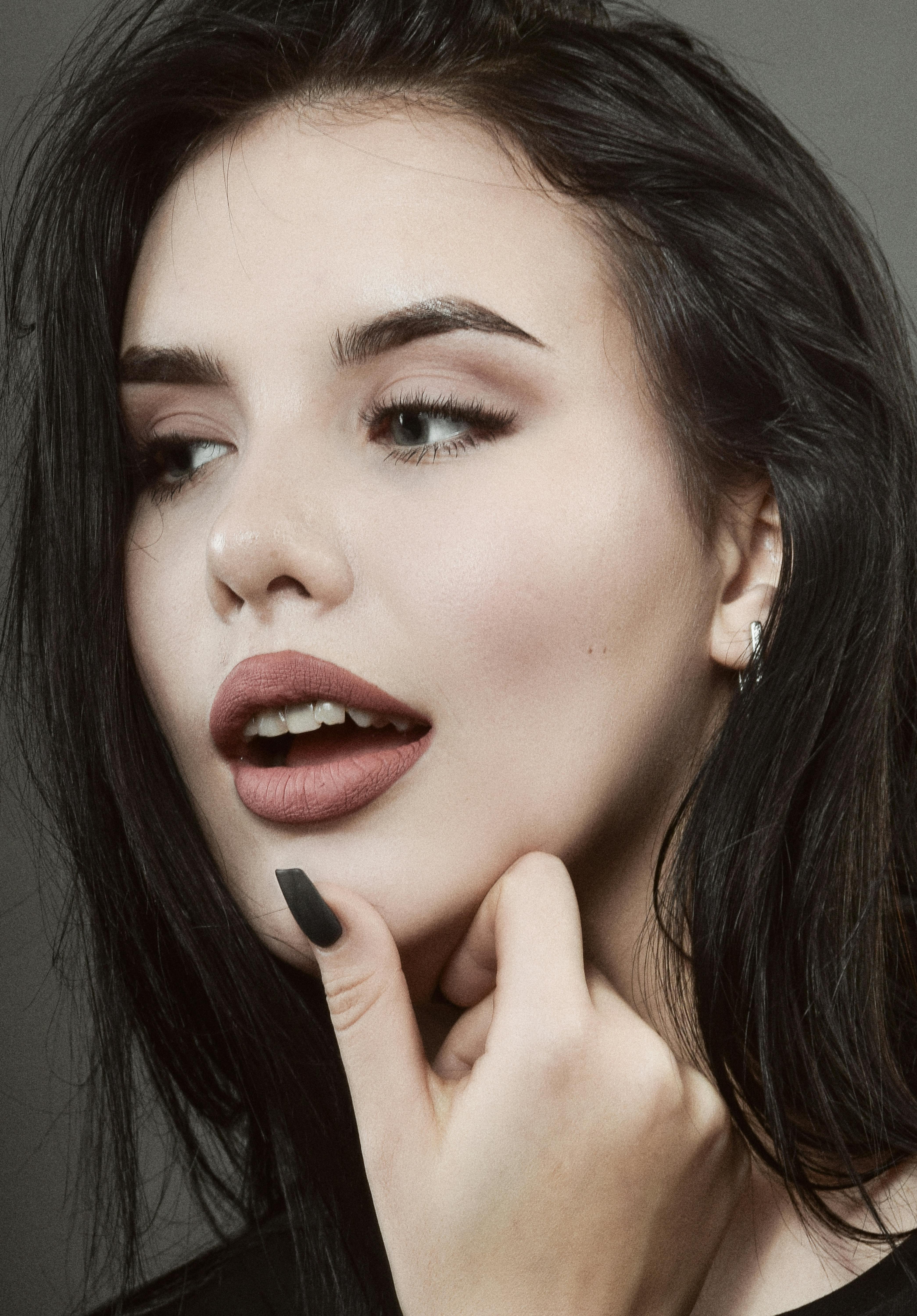 Close-up portrait of a woman with dark hair, lipstick, and hand near chin.