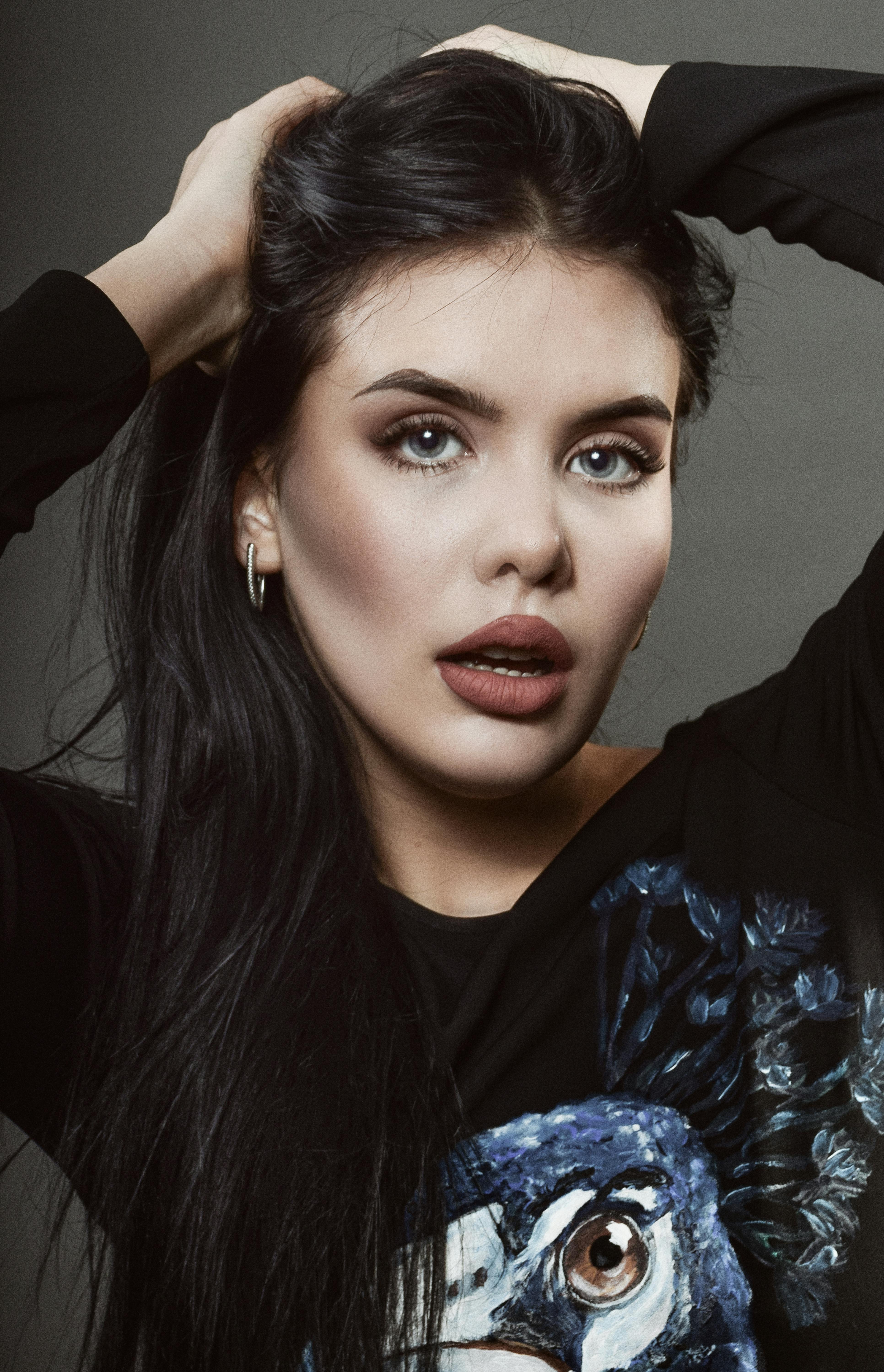 Fashion portrait of a woman with long black hair and expressive eyes against a gray background.