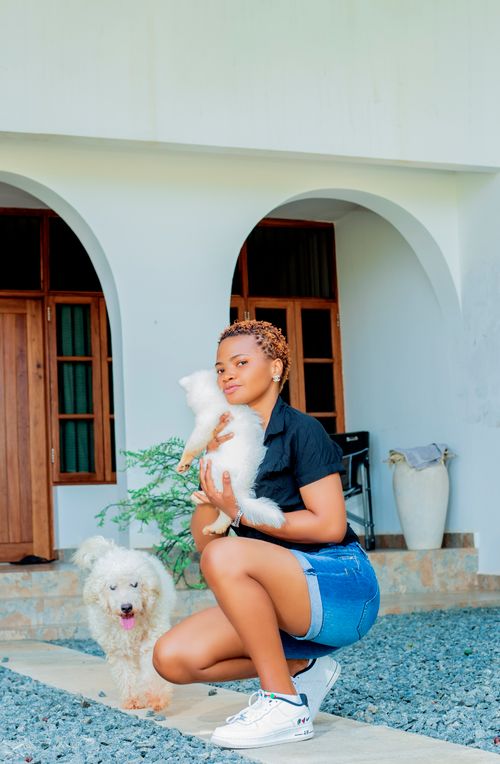 Free A young woman crouching with two fluffy white dogs outside a house. Stock Photo