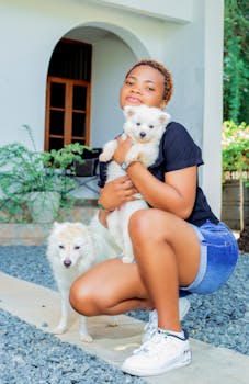Stylish woman crouching with two dogs outdoors, showcasing fashion and pets.