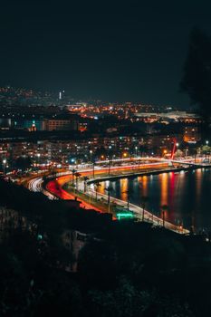 Vibrant nighttime view of İzmir's coastline with city lights reflecting on water.