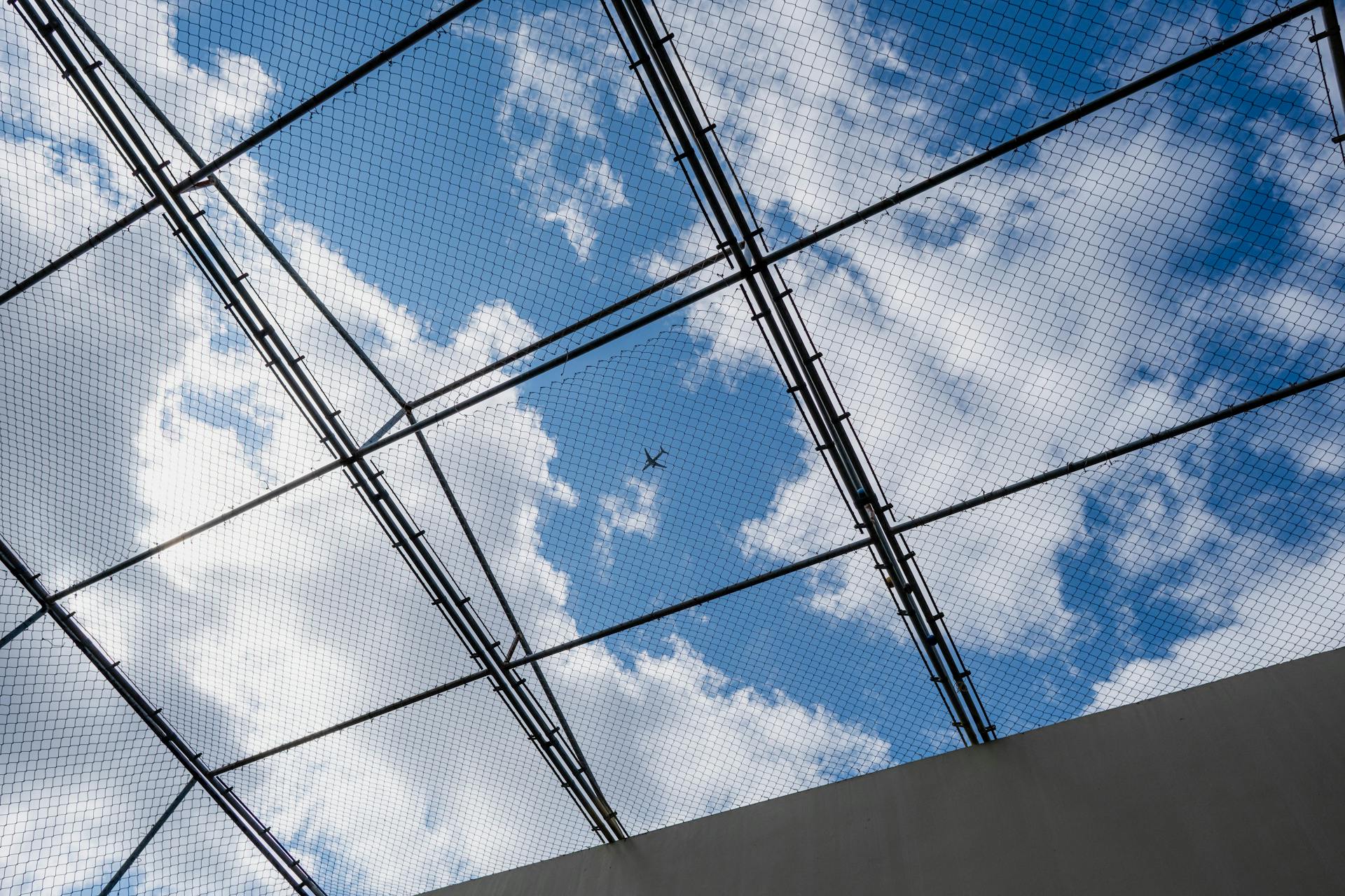 View of an airplane flying above a grid structure with a clear blue sky and clouds.