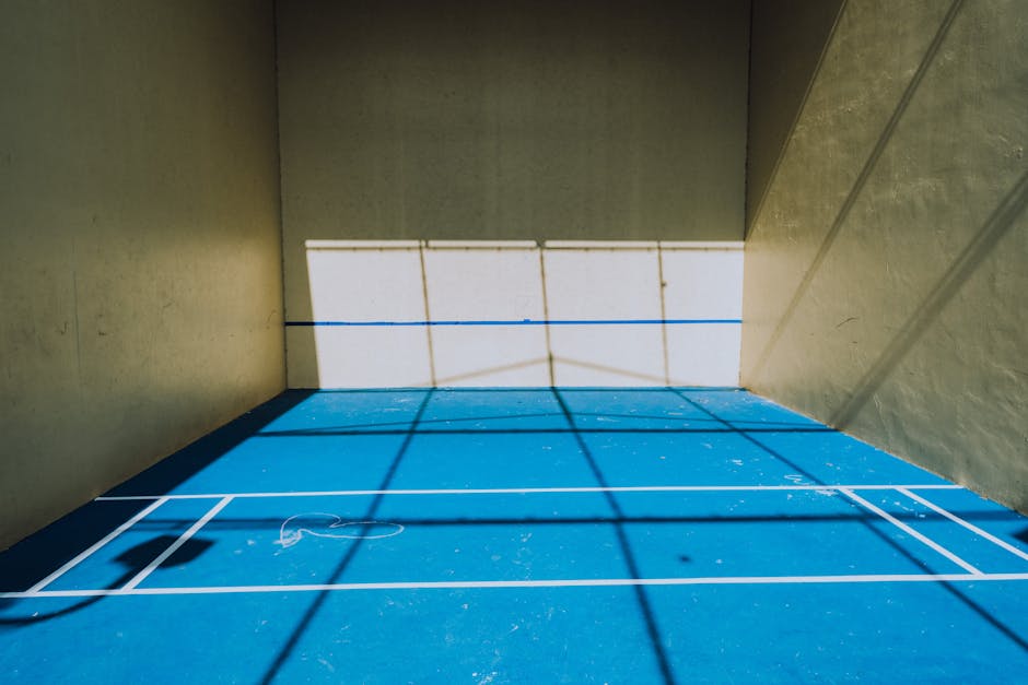 A pickleball court illuminated by sunlight, creating unique shadow patterns on the blue floor.