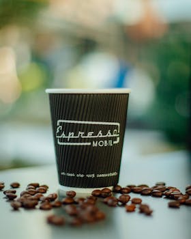 Disposable coffee cup surrounded by coffee beans on a blurred background, perfect for food photography.
