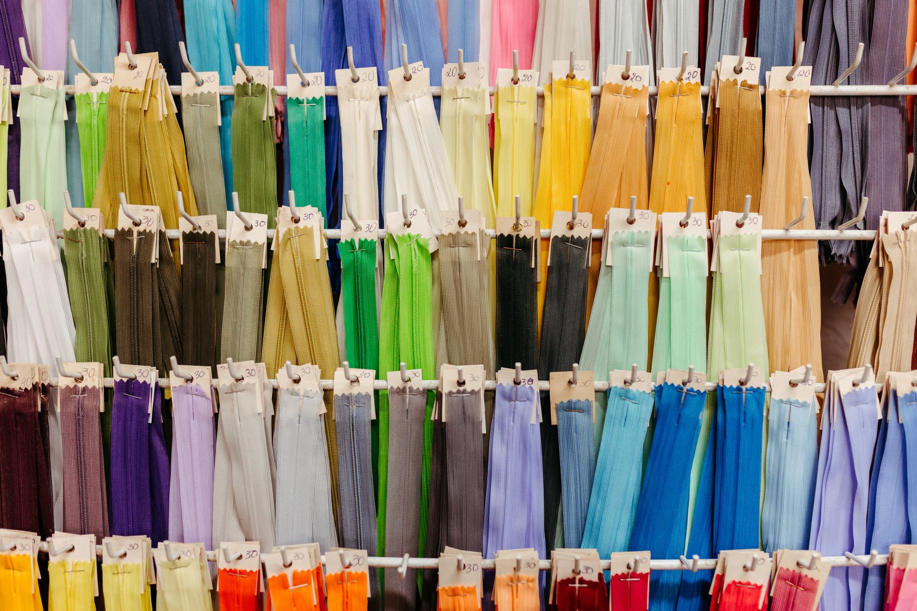 A vibrant collection of zippers in various colors neatly hanging on display hooks.