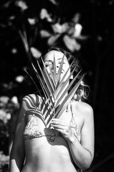 Artistic black and white portrait of a woman holding a palm leaf outdoors.