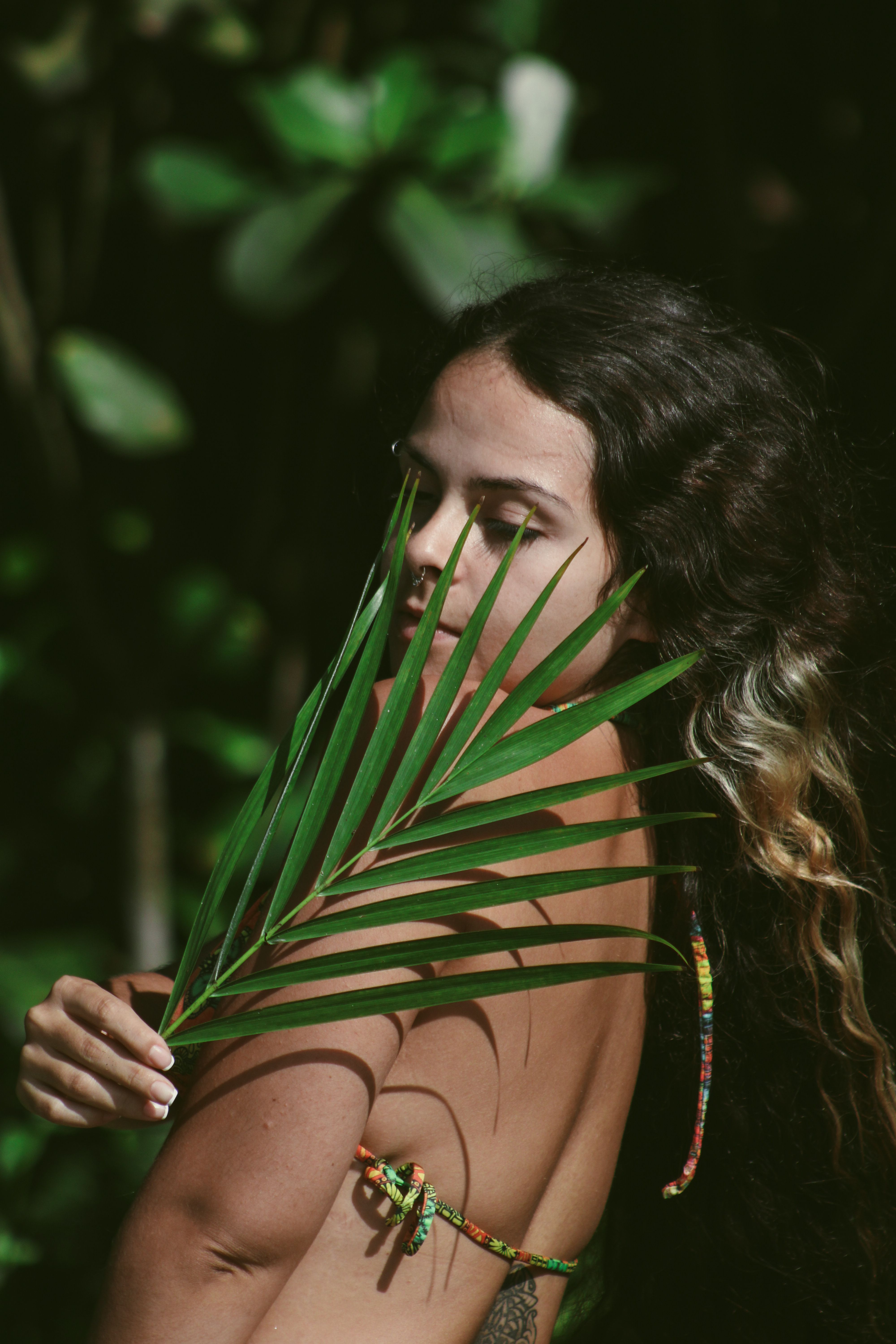 Sunlit portrait of a woman posing with a green leaf outdoors.