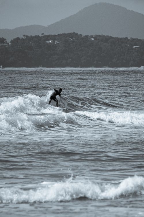 Free A solitary surfer expertly rides the waves on a picturesque coastline with a mountain backdrop. Stock Photo