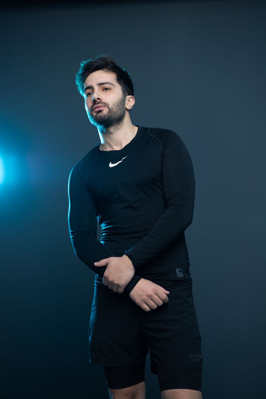 Stylish portrait of a man posing with confidence in black sportswear on a blue background.