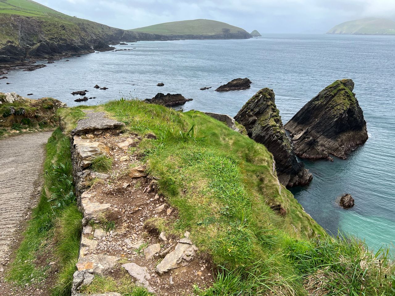 A grassy footpath running along the top of the sea cliffs at Dunquin on the Dingle Peninsula, with rock stacks and headlands beyond
