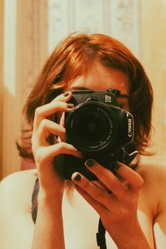 A redhead woman captures a mirror selfie with her camera in an indoor setting. Perfect for lifestyle and photography themes.