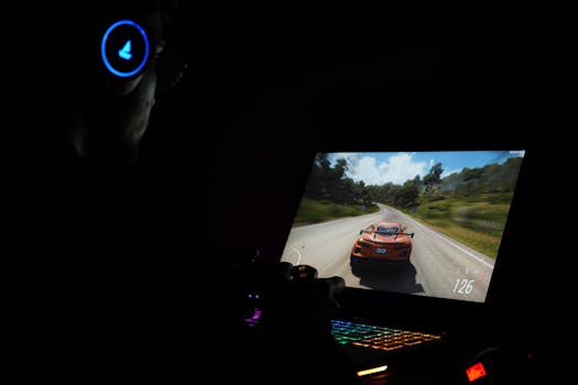 A gamer using a laptop and headphones to play a car racing game in a dark setting.