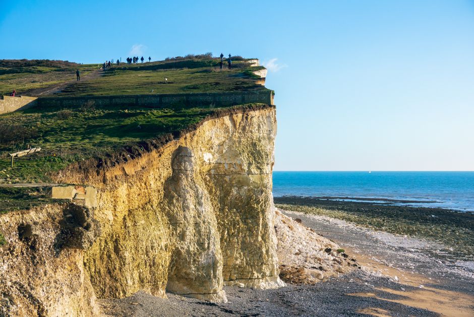 Stunning view of a coastal cliff with people sightseeing, clear skies, and blue ocean.