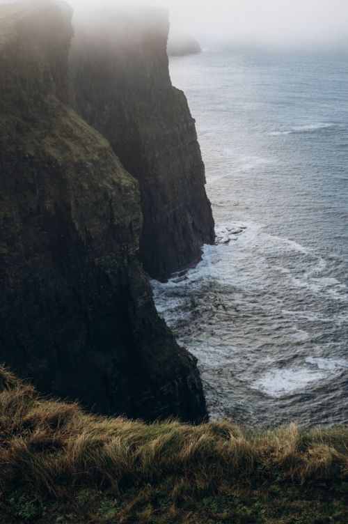 Free Majestic cliffs meeting the sea, enveloped in mist, creating a serene and dramatic coastal scene. Stock Photo