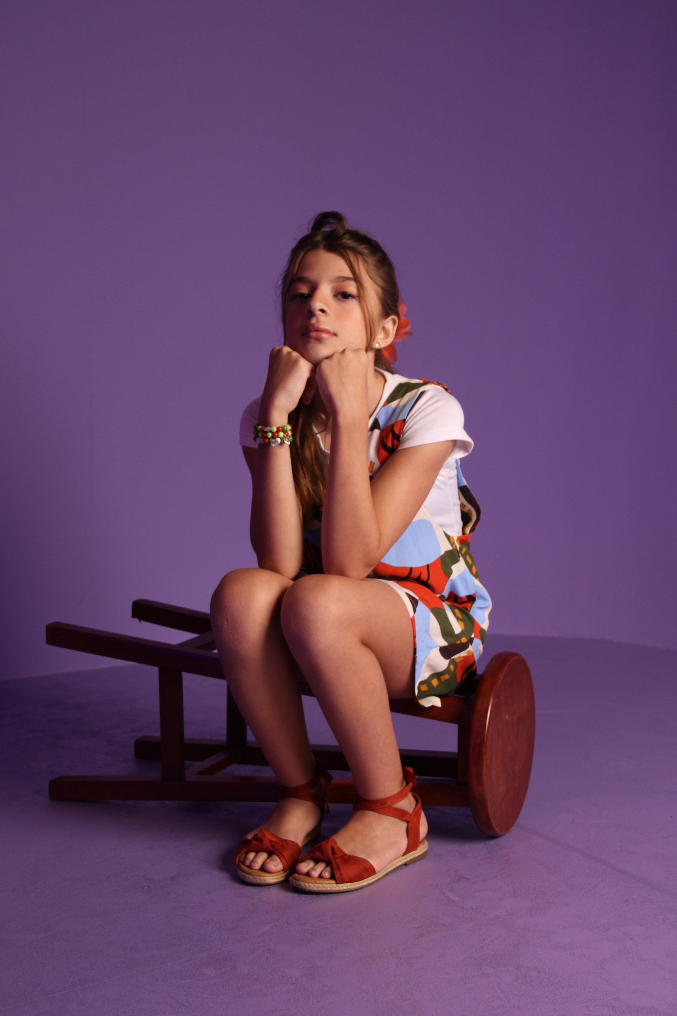 A young girl posing stylishly in a studio with a purple backdrop, exuding confidence.