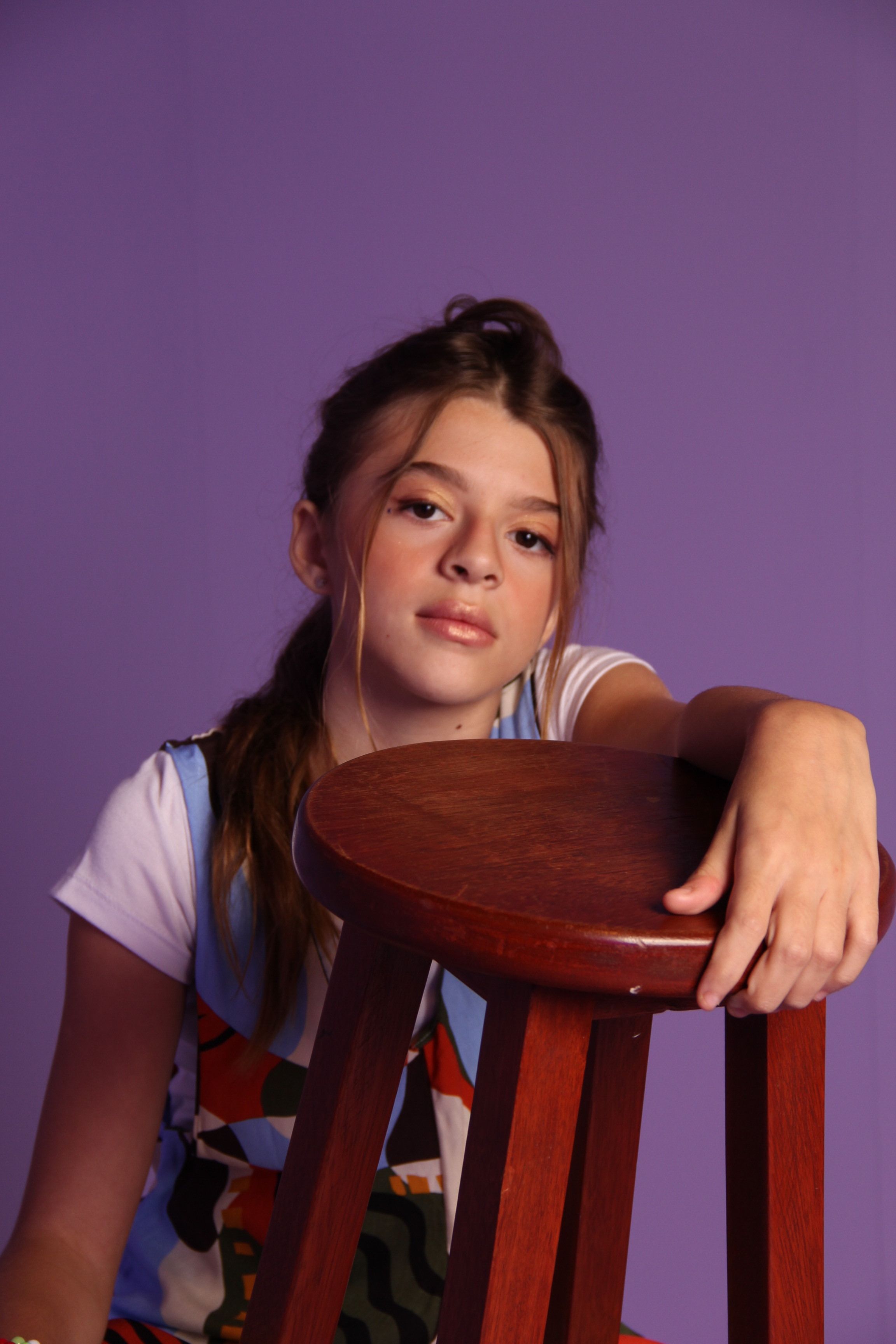 Portrait of a teenager posing with a wooden chair against a purple background.