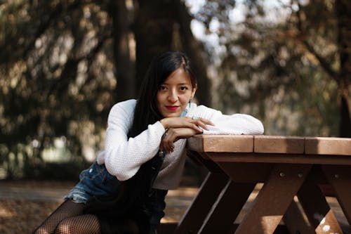 Woman in White Sweater Sitting on Wooden Picnic Table