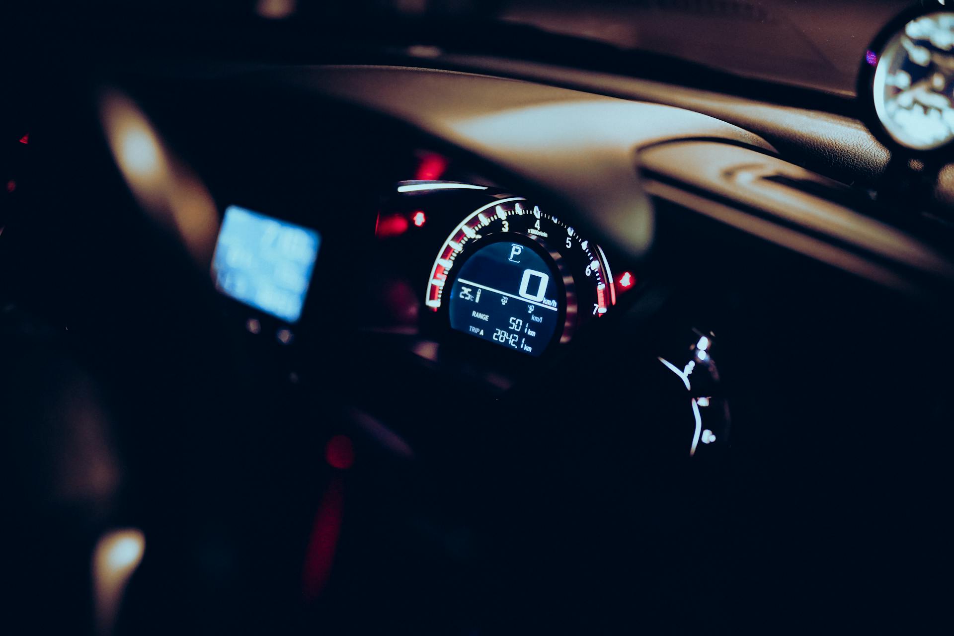 Close-up of a car dashboard at night with illuminated speedometer and tech displays.