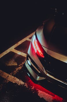 Close-up of a modern sports car in a dimly lit parking lot, highlighting the sleek headlights.