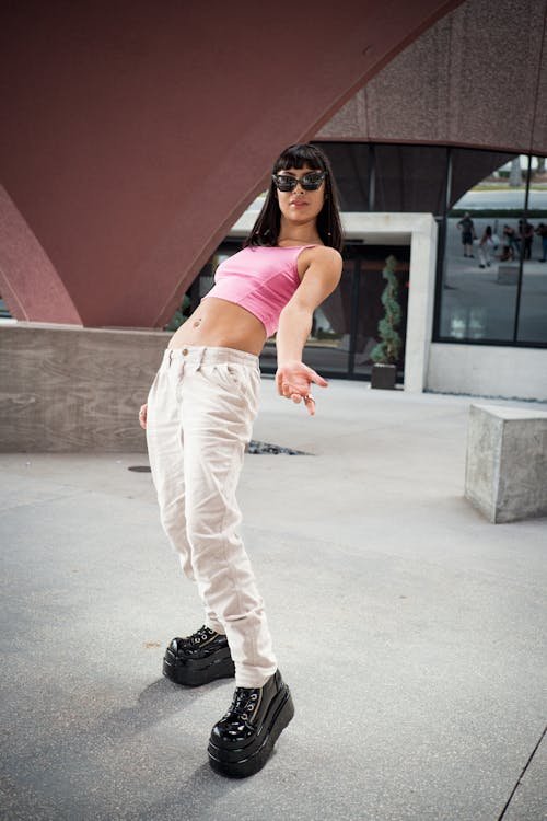 Young Woman in a Casual Outfit and Sunglasses Standing in front of a Building in City and Leaning Backwards 