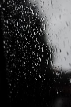 A monochrome image capturing raindrops on a glass window, emphasizing texture and mood.