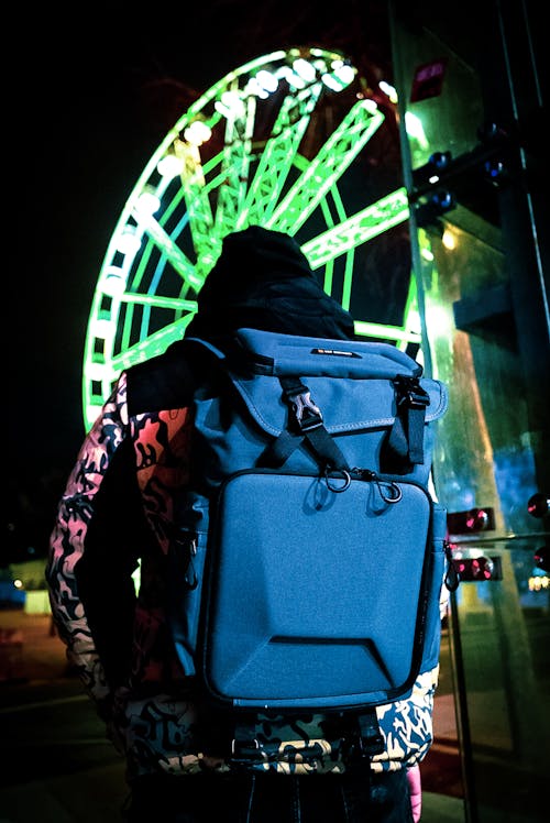 Back View of a Man with a Jacket Standing near an Illuminated Ferris Wheel at Night 
