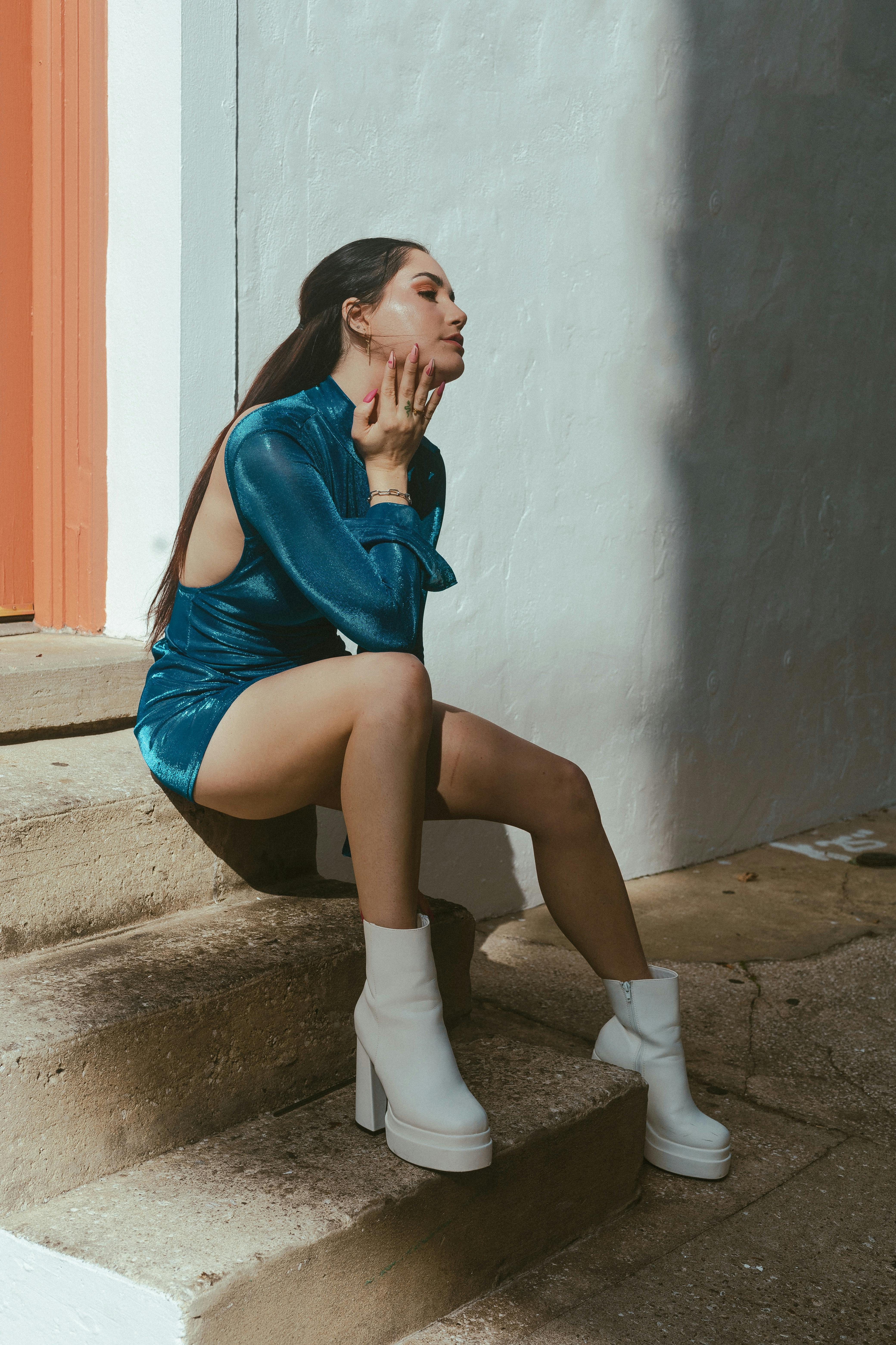 Free Stylish woman in blue dress and white boots sitting on concrete steps, striking a thoughtful pose. Stock Photo