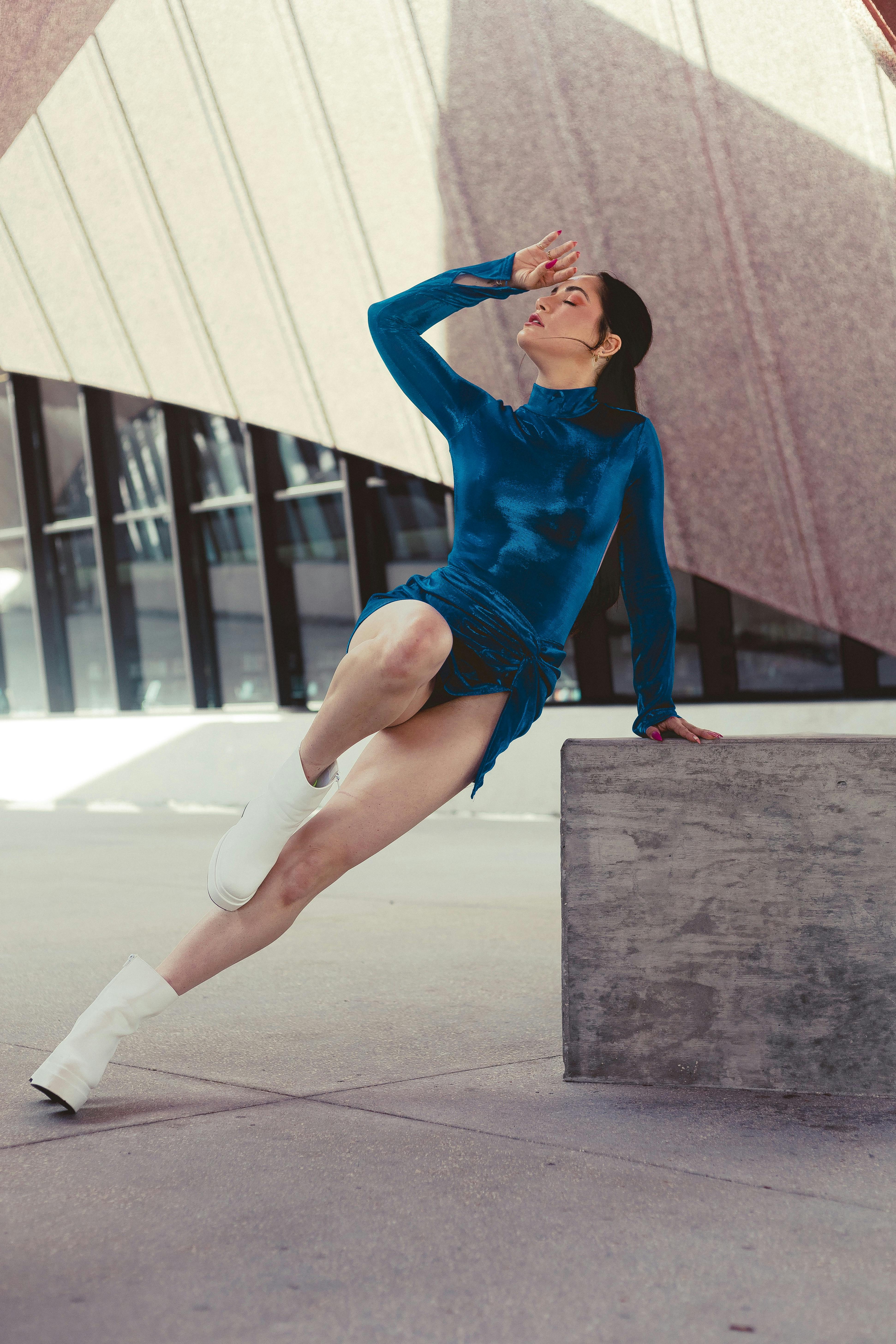 A woman in a blue dress poses gracefully in an urban setting, showcasing modern fashion.