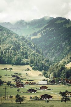 Picturesque view of a peaceful village nestled in the Swiss Alps with lush green hills and mountains.