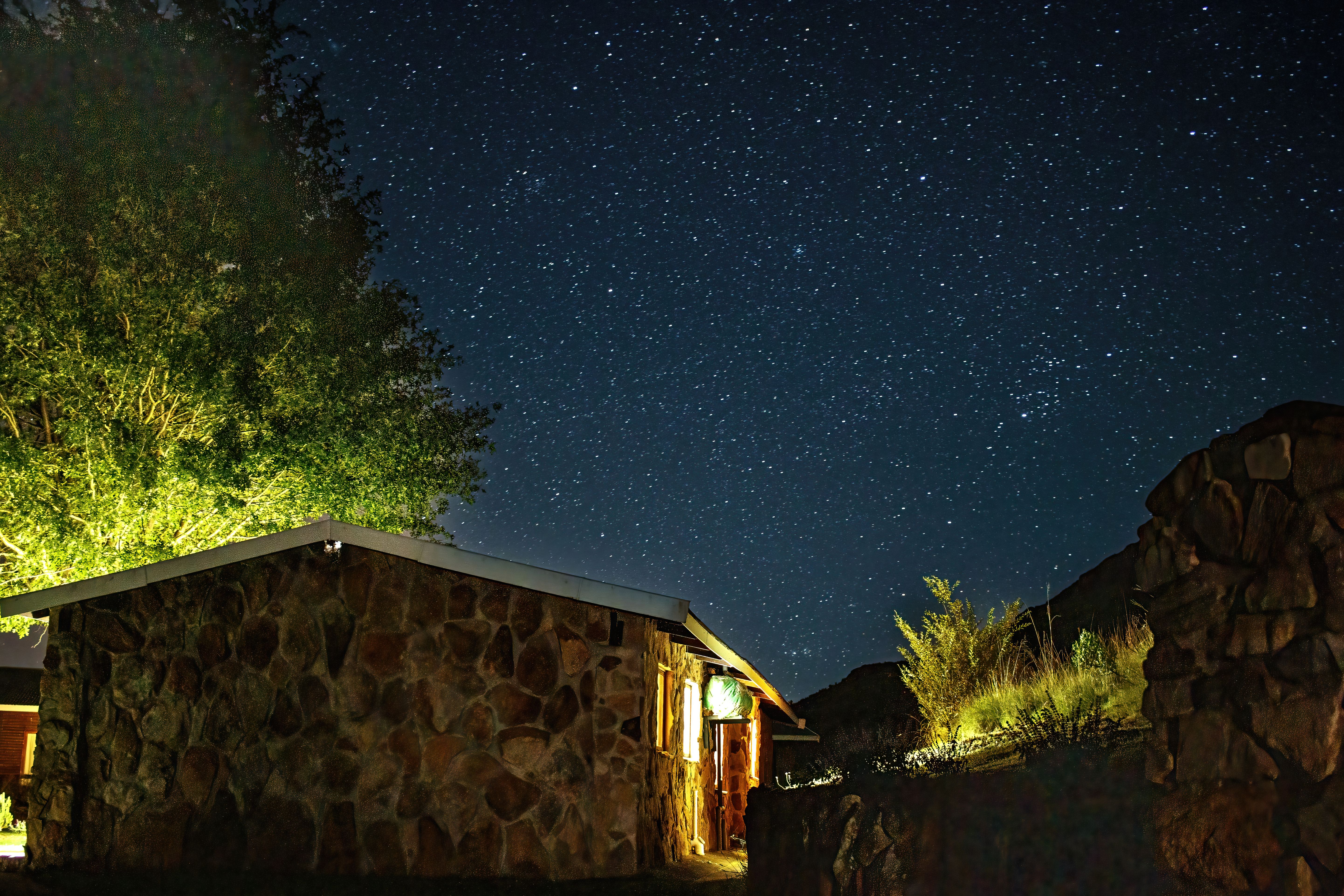 View of a Starry Night Sky over a Stone House and Trees · Free Stock Photo