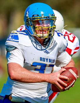 Close-up of player in blue helmet running with a football on a sunny field.
