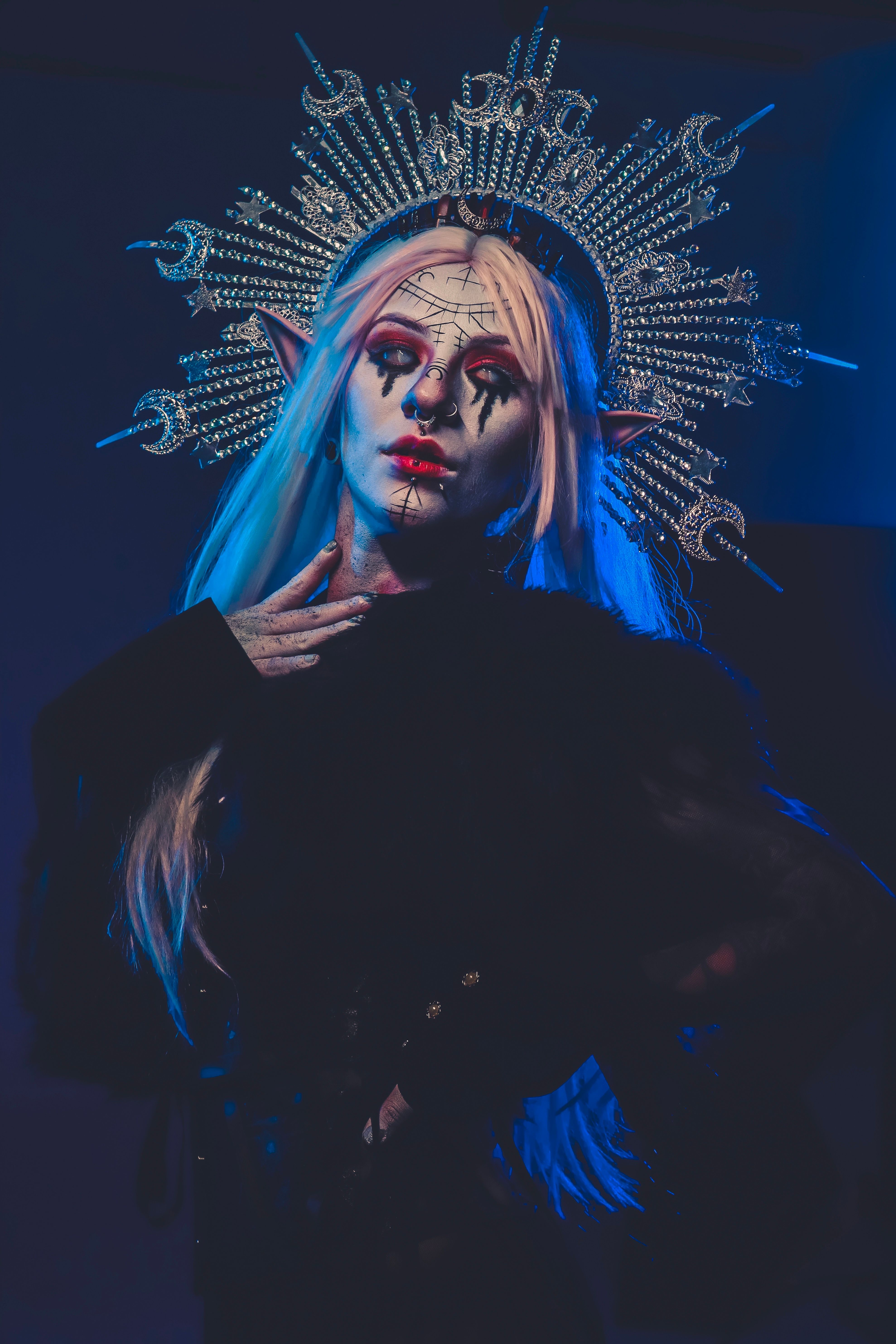 A woman in Halloween makeup poses in a studio with a dramatic headpiece and wig, creating a fantasy character.