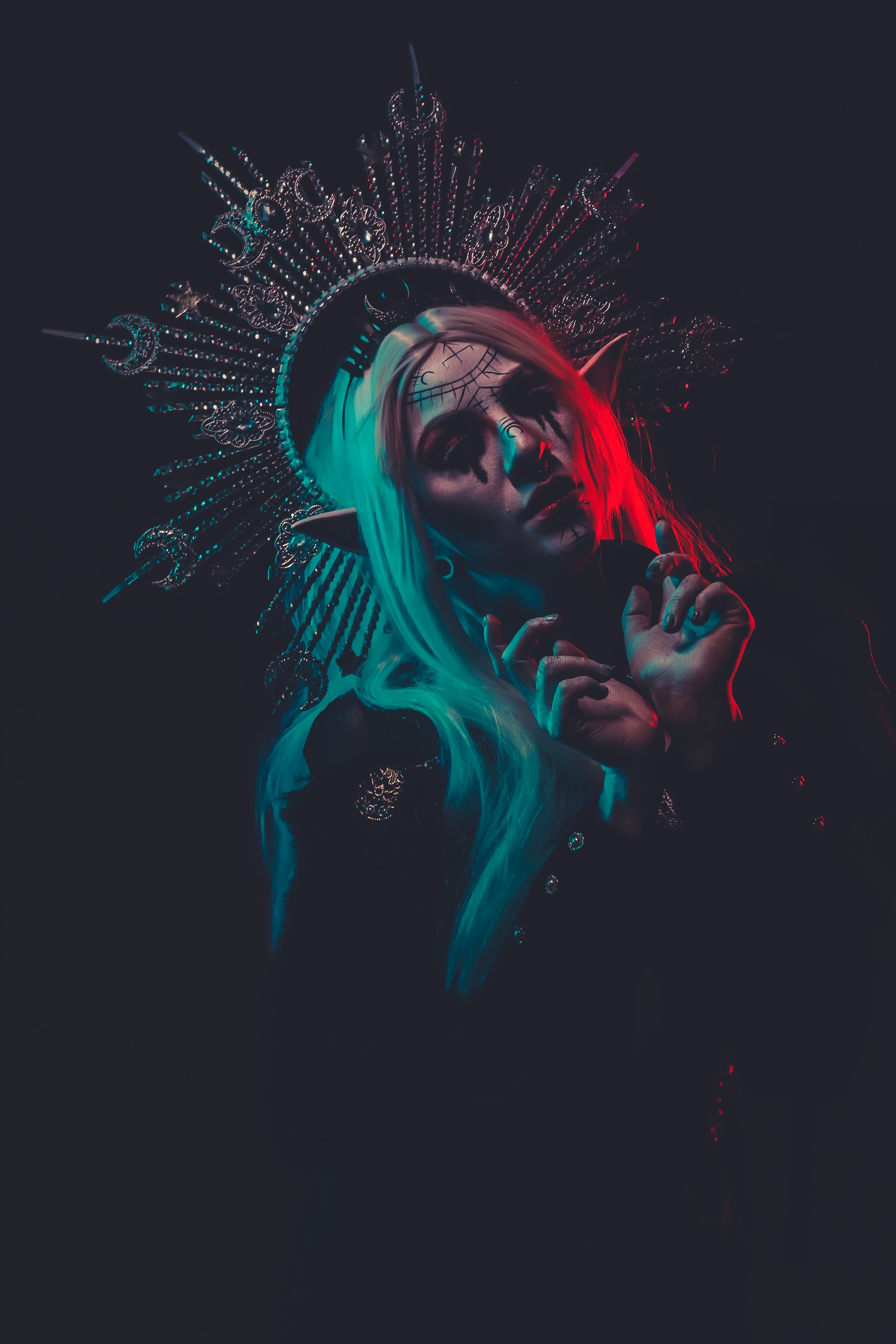 A woman with artistic makeup and a dramatic headdress exudes mystery in moody lighting.