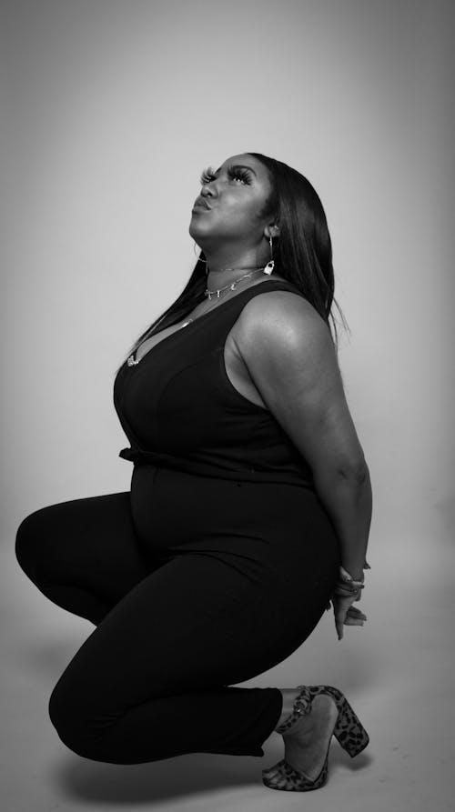 Black and White Studio Shot of a Woman in a Jumpsuit and Heels Crouching and Looking Up