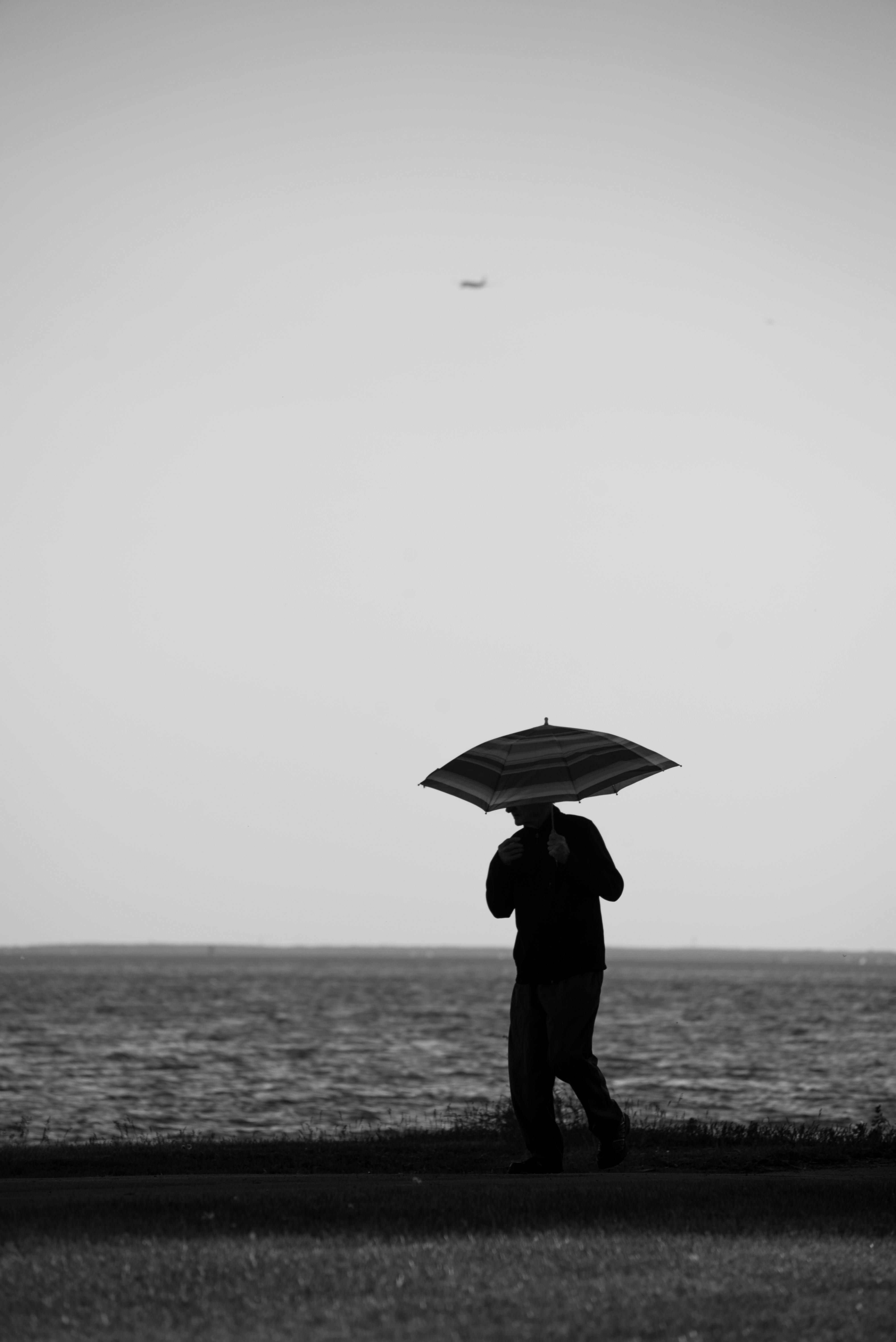 Grayscale Photo of a Man with an Umbrella near the Beach · Free Stock Photo