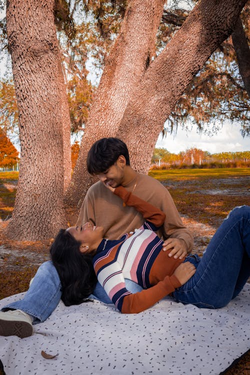 Young Couple Lying on a Blanket in a Park and Smiling 