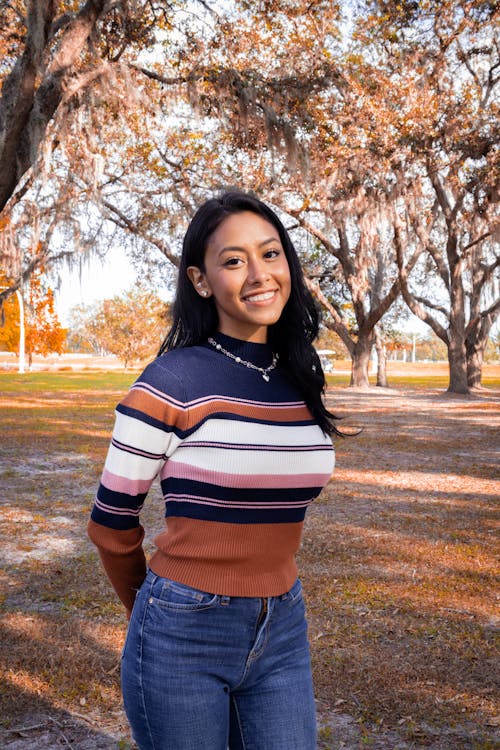 Young Woman in Jeans and Striped Sweater Standing in a Park in Autumn 