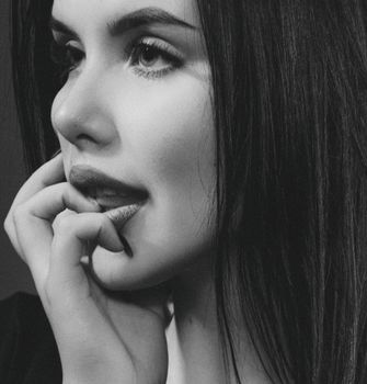 Stunning black and white close-up portrait of a young woman with hand on lips.