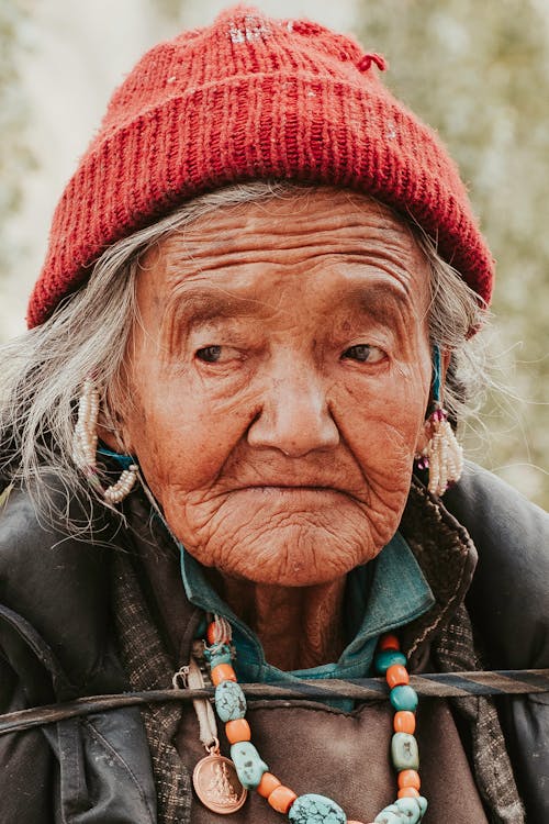 Close-Up Photo of an Old Woman Wearing Red Knit Cap