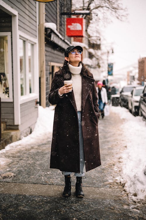 A Woman Standing on the Sidewalk While Snowing 