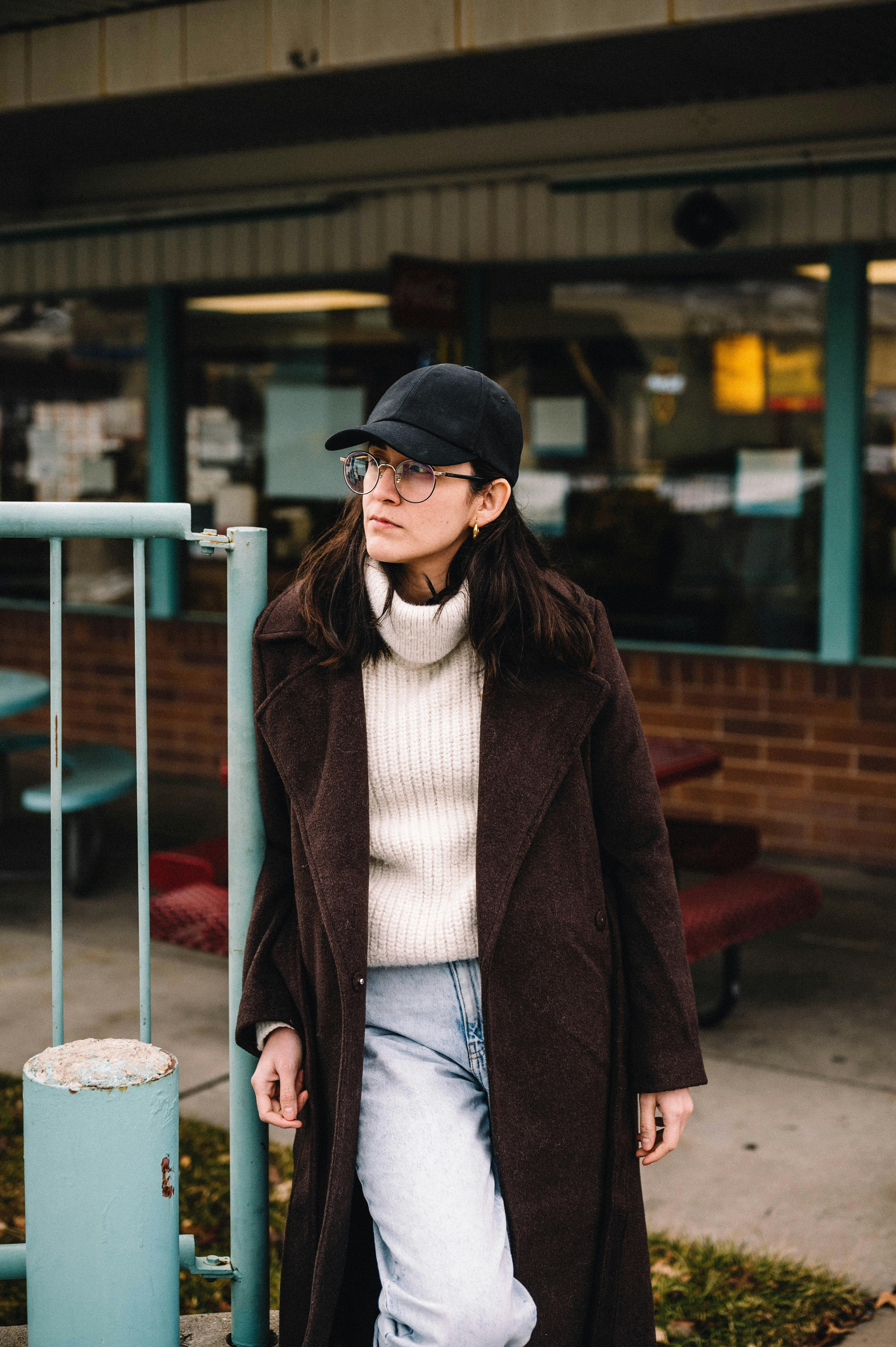 Free Chic woman wearing a cap and eyeglasses, stylishly posing outdoors in urban attire. Stock Photo
