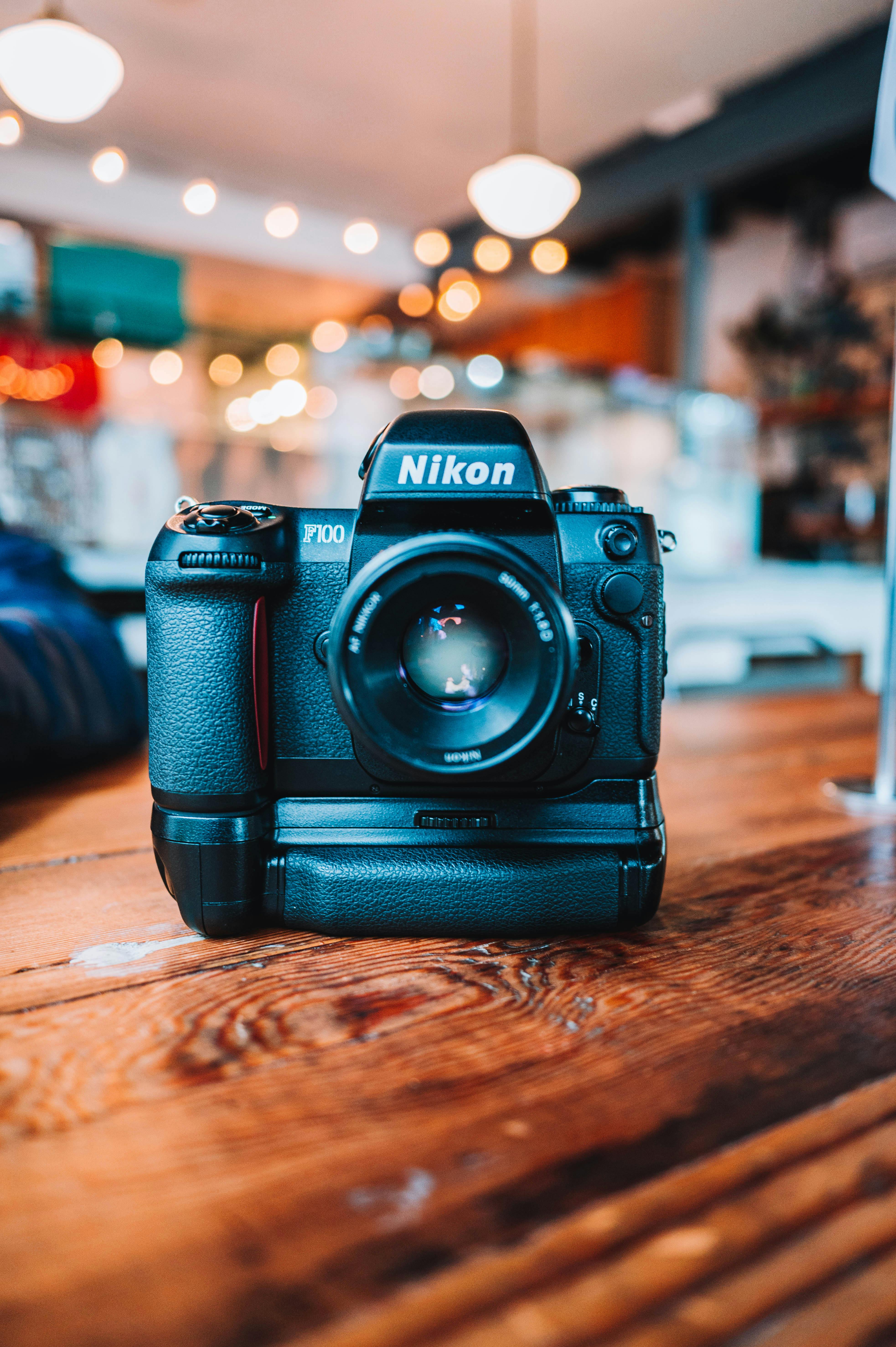 Free A close-up view of a vintage Nikon camera on a wooden table in a cozy café with blurred background. Stock Photo
