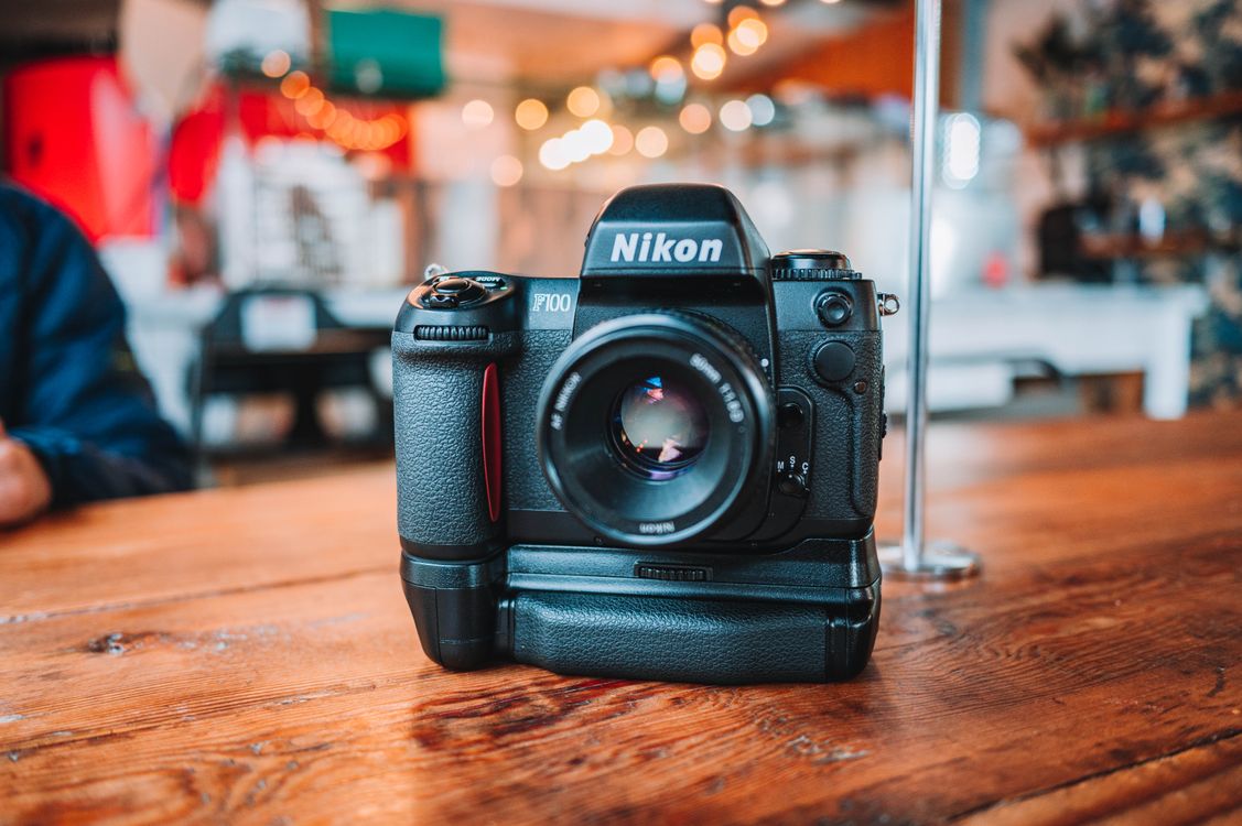 Close-up of a Nikon F100 Camera Standing on a Wooden Table · Free