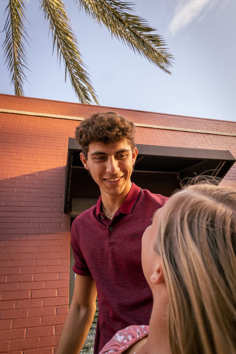 A Couple Standing Outside Beside A Building And Palm Tree And Smiling 