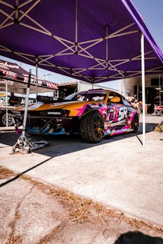 A colorful racing car parked under a purple canopy at a motorsport event, showcasing vibrant designs.