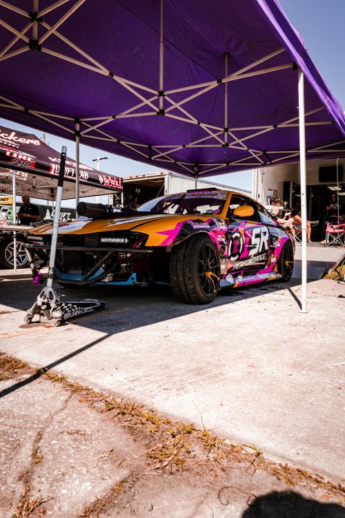 Free A colorful racing car parked under a purple canopy at a motorsport event, showcasing vibrant designs. Stock Photo