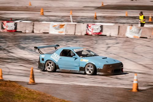 Free A blue sports car performing a drift maneuver on a race track with spectators nearby. Stock Photo