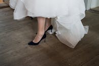 新娘穿着黑色高跟鞋的脚，特写于木地板上的白色婚纱下